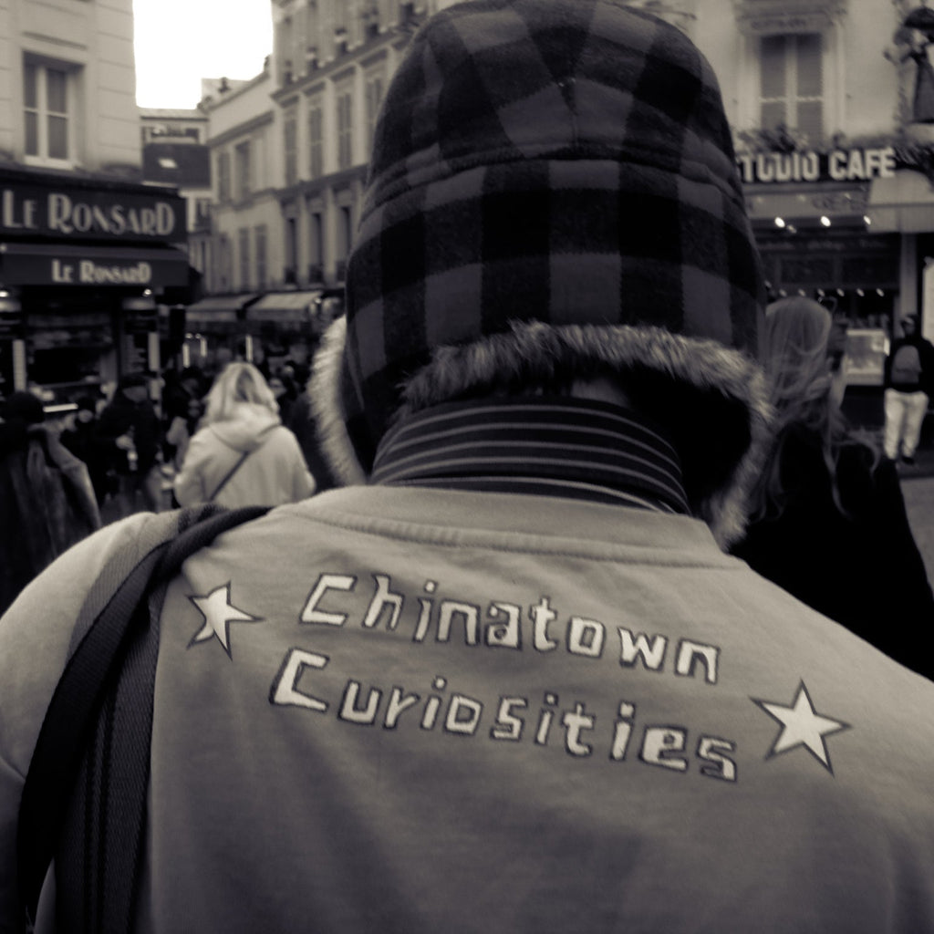 Person wearing a jacket with 'Chinatown Curiosities' text on a busy street.